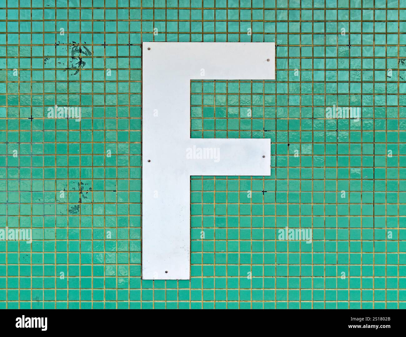 Buchstabe F in weiß auf einer gekachelten grünen Wand Stockfoto
