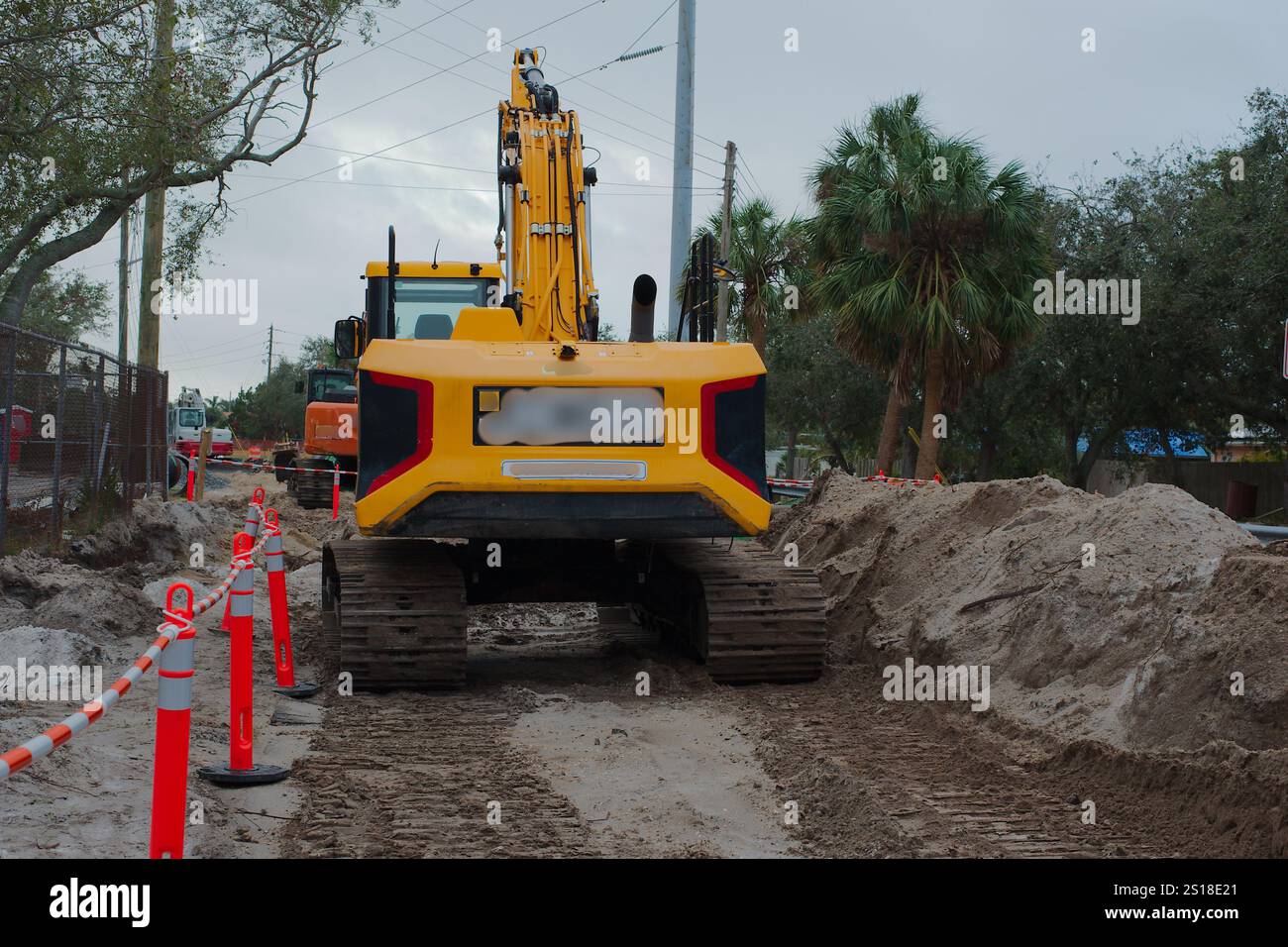 Weiter Blick hinter einer Baustelle mit einem gelben Raupenbagger. Orangefarbene Zaunkegel mit führenden Schmutzlinien zu anderen Geräten. Stockfoto