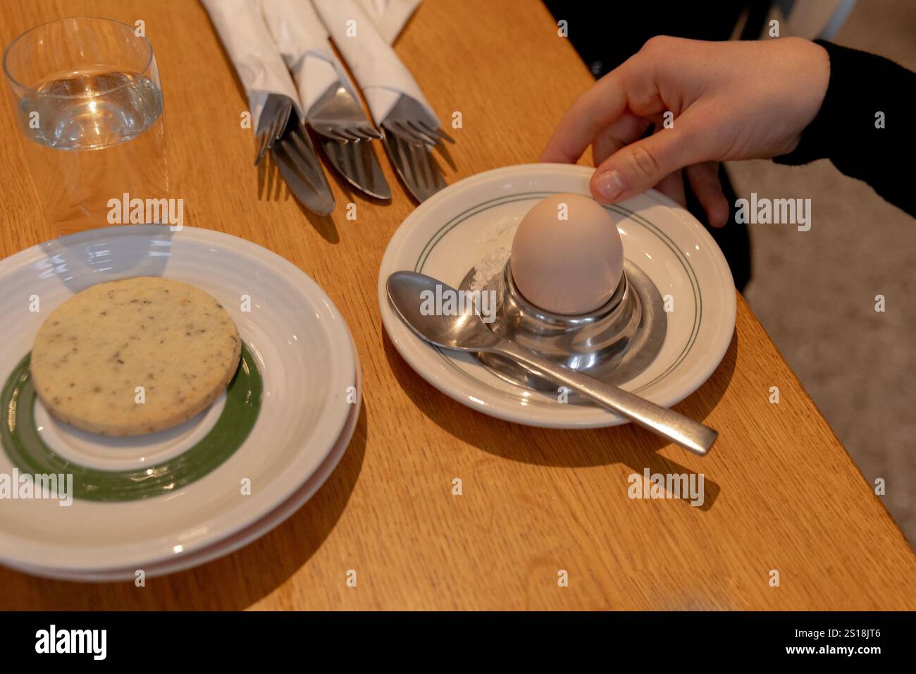 Frühstück auf dem Tisch, ein gekochtes Ei, eine Hand, die einen Teller hält, Kekse auf einem Teller Stockfoto