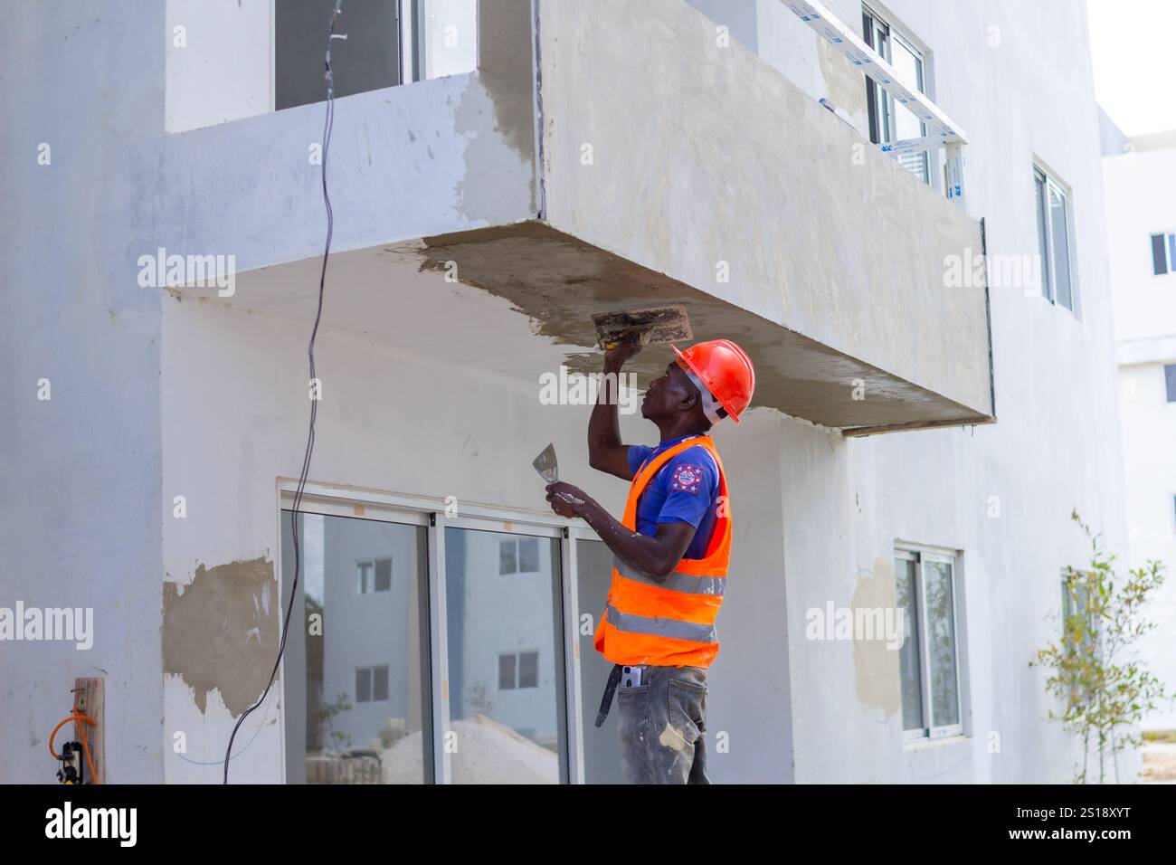 SANTO DOMINGO, DR - 4. Februar 2021: afroamerikanischer Mann, der im Wohnungsbau arbeitet und Zement in einem hohen Bereich der Baustelle aufbringt Stockfoto