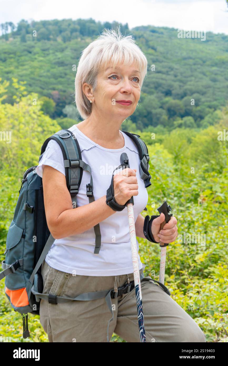 Eine 60-65-jährige Frau läuft mit Nordic-Walking-Stangen durch den Wald. Stockfoto