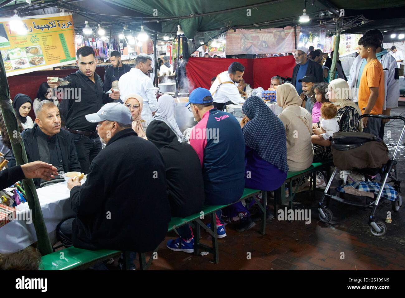 Die Einheimischen sitzen auf Bänken und essen abends an einem der Imbissstände auf dem jemaa el-fna-Platz marrakesch, marokko Stockfoto