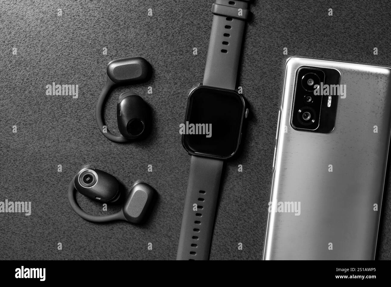 Kabellose Kopfhörer mit offenem Ohr, Smart Watch und Mobiltelefon auf grauem Steintisch, Nahaufnahme, Draufsicht Stockfoto