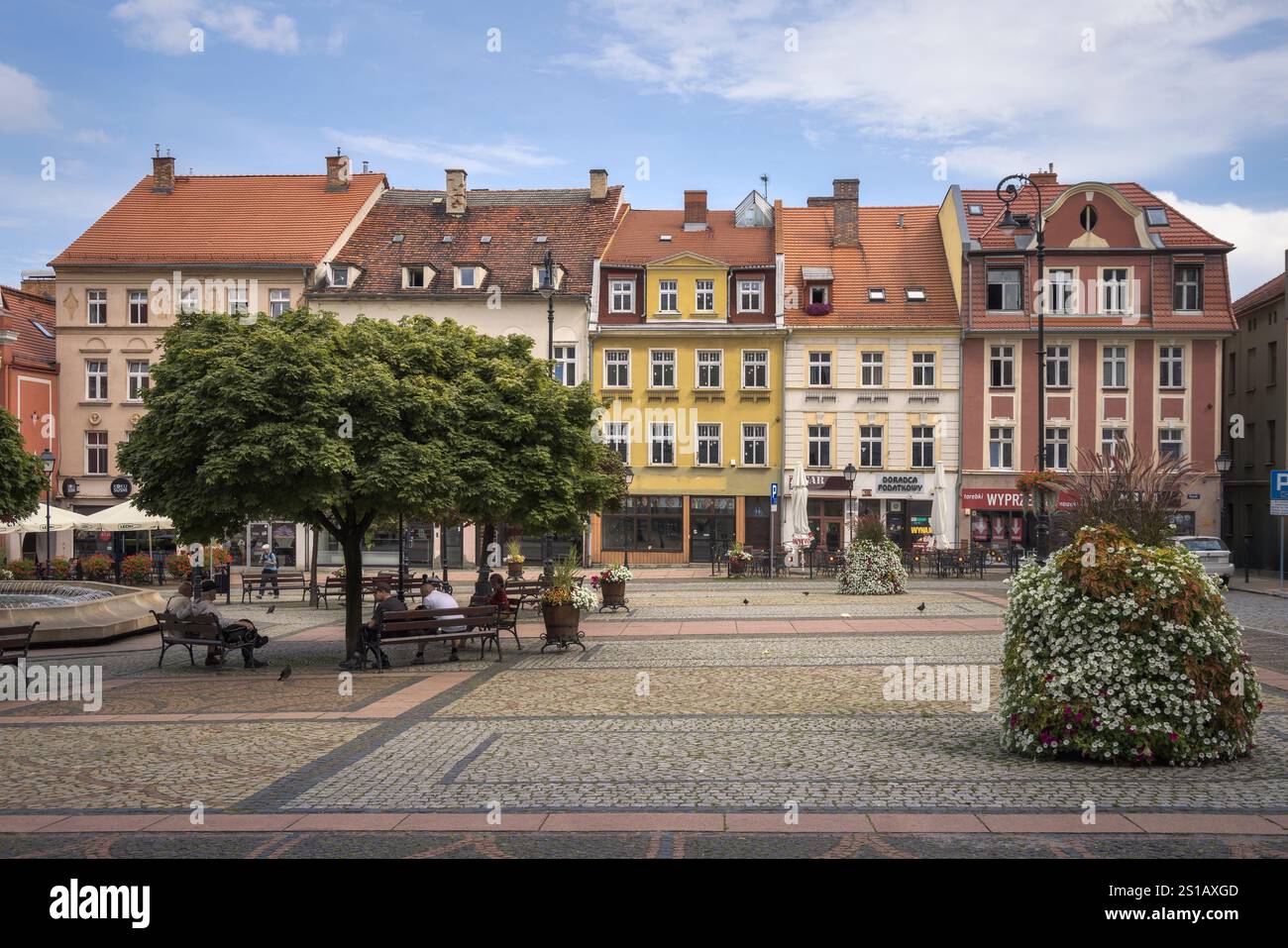 Besucher genießen an einem sonnigen Tag in Polen Freizeit auf Walbrzychs malerischem Platz mit farbenfrohen Gebäuden und üppigen Bäumen Stockfoto