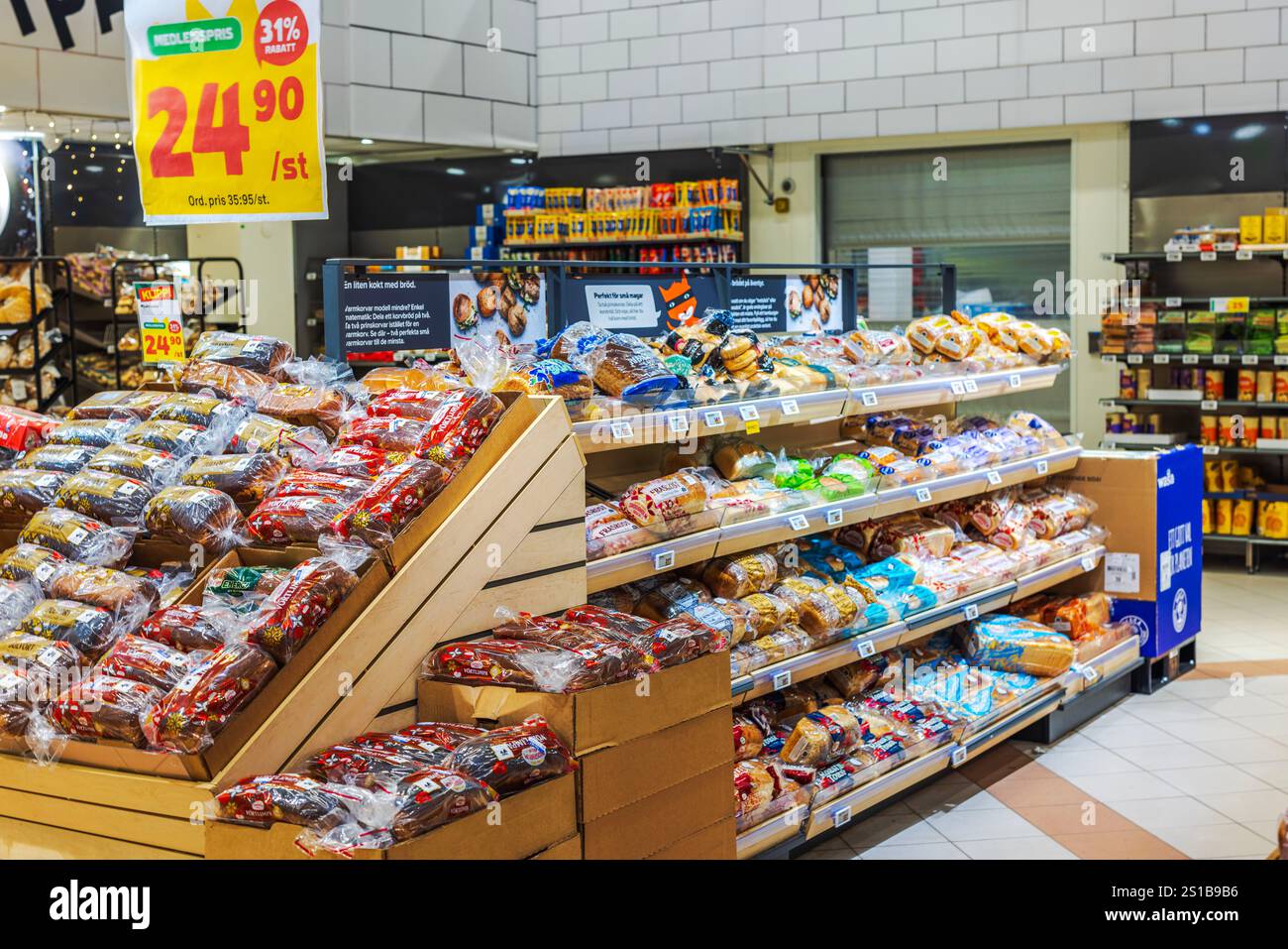 Verschiedene verpackte Brote auf Holzregalen in der Bäckerei des Lebensmittelgeschäfts mit hellen Werbeschildern. Stockfoto