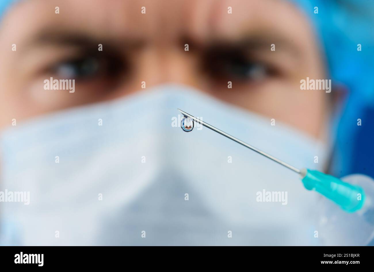 Tropfen des Arzneimittels auf die Spitze der medizinischen Injektionsnadel. Arzt in medizinischer Maske mit Spritze Vorbereitung auf die Injektion. Impfstoffentwicklung. Tropfen Flüssigkeit Stockfoto