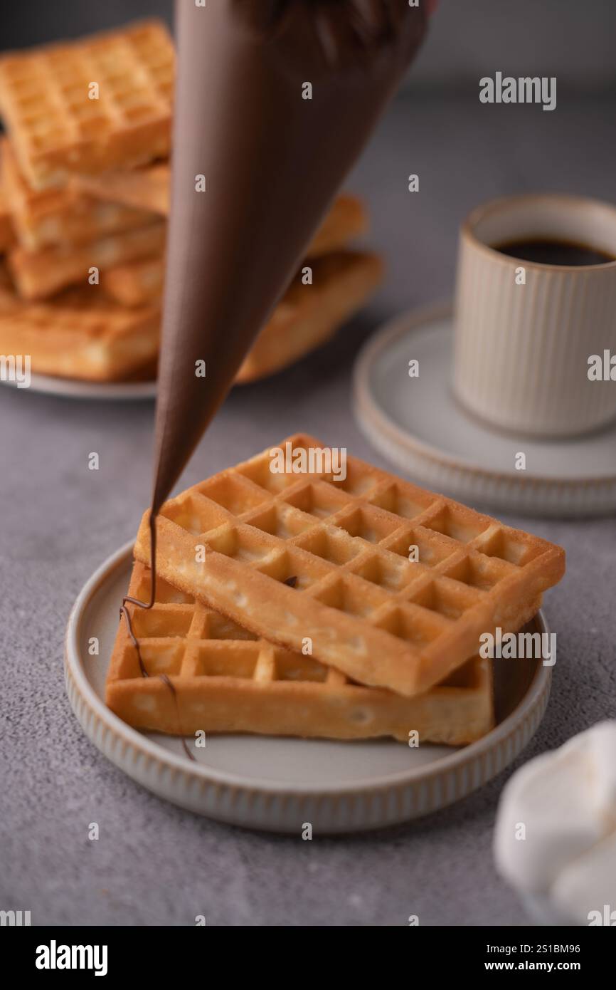 Machen Sie Fotos von köstlichen hausgemachten Waffeln mit Schokoladennebel und Kaffee für ein köstliches Frühstückserlebnis oder einen Brunch, der Ihren süßen Geschmack erfüllt Stockfoto