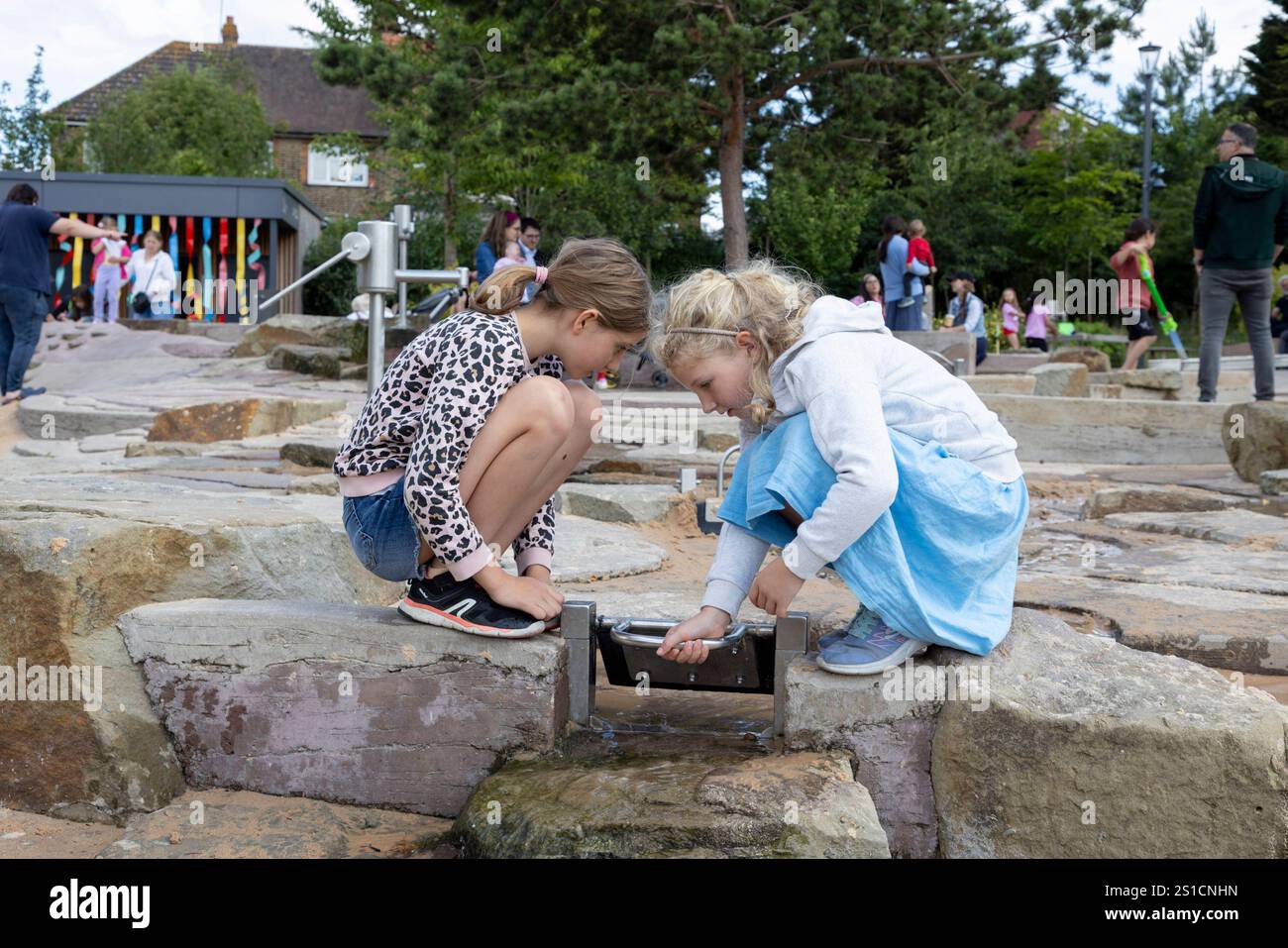 Zwei Schwestern, 8 und 7, spielen mit einem Wasserspiel auf einem Spielplatz in Brent Cross Town, einem Bauprojekt in NW London Stockfoto