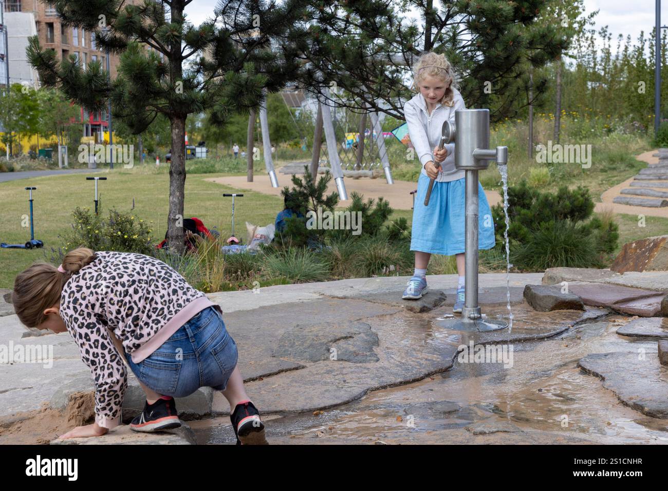 Zwei Schwestern, 8 und 7, spielen mit einem Wasserspiel auf einem Spielplatz in Brent Cross Town, einem Bauprojekt in NW London Stockfoto
