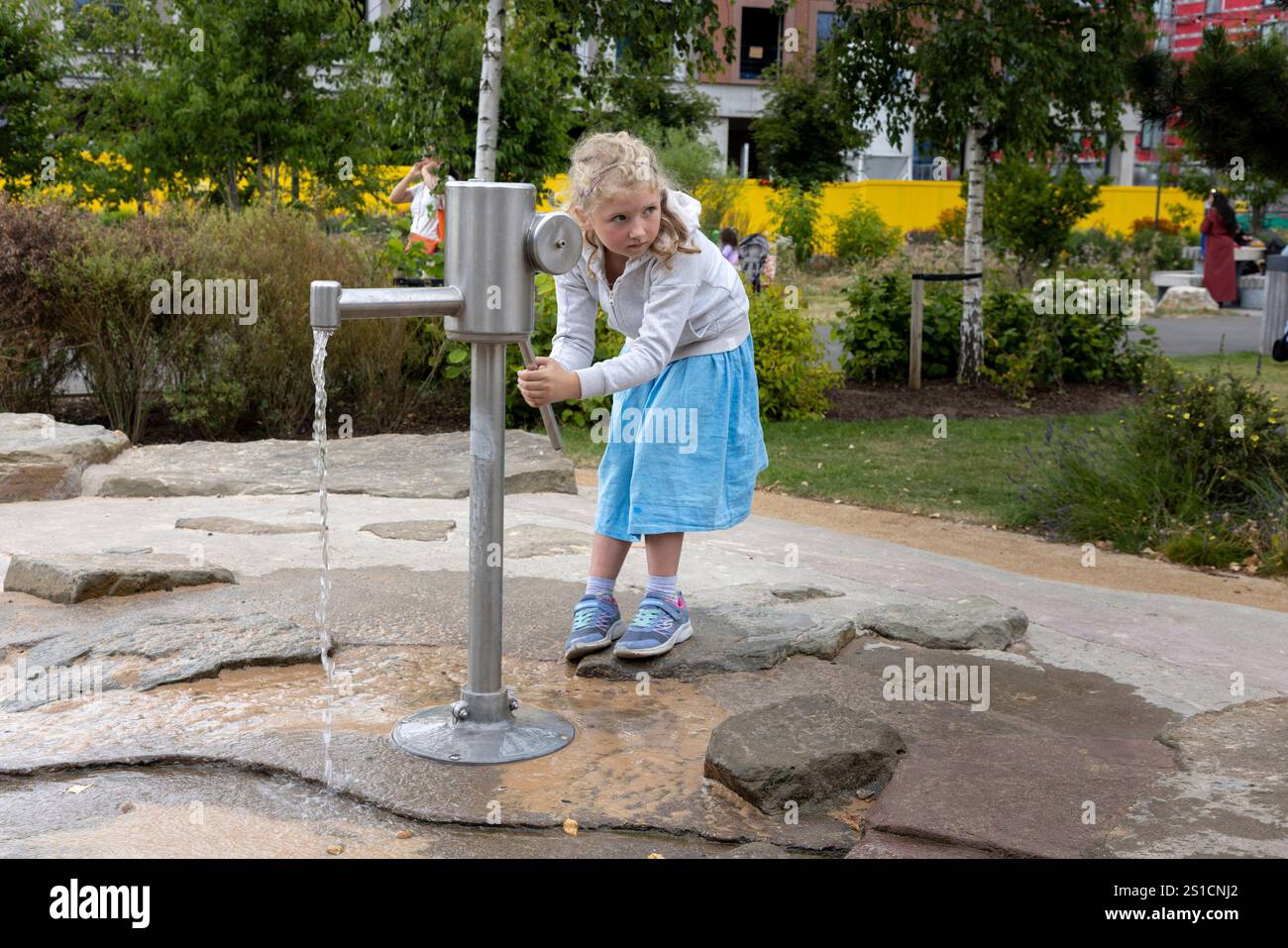 Ein 7-jähriges Mädchen spielt mit einer Wasserpumpe auf einem Spielplatz in Brent Cross Town, einem Bauprojekt in NW London Stockfoto