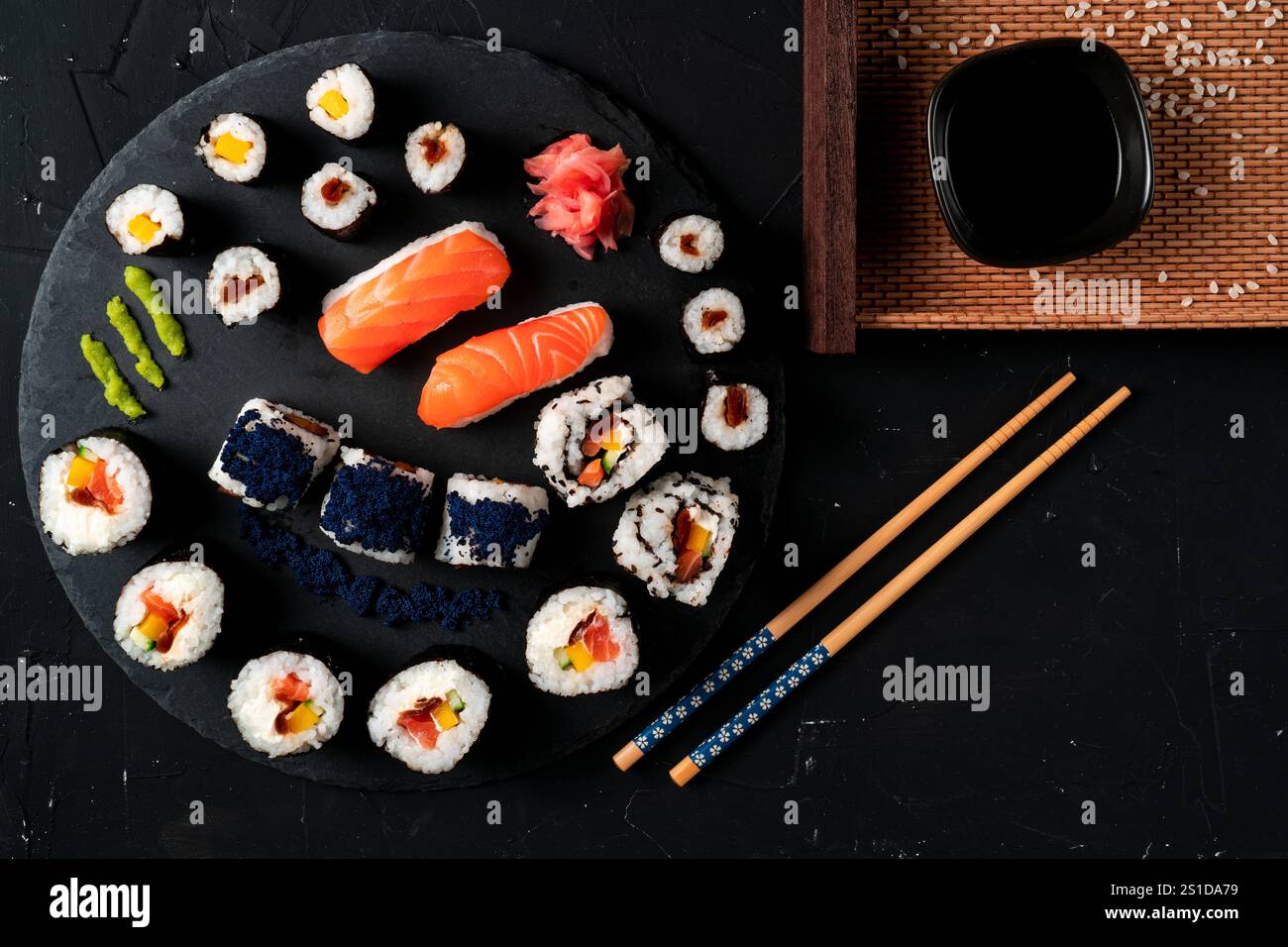 Sushi-Board mit Sojasauce und Essstäbchen. Japanisches Essen auf schwarzem Teller und schwarzem Hintergrund. Ein typisch japanisches Essen. Stockfoto