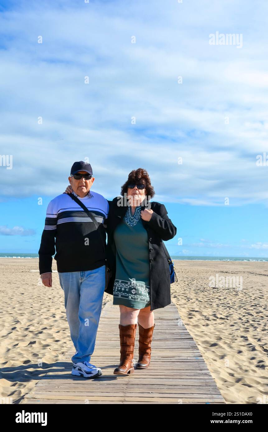 Seniorenpaar, das einen gemütlichen Spaziergang auf einer sonnigen Strandpromenade genießt Stockfoto