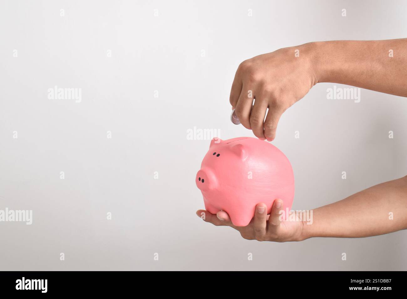 Hand, die Münzen in die Schweinebank auf weißem Hintergrund platziert. Geld sparen für Altersvorsorge und Zukunftskonzept. Stockfoto