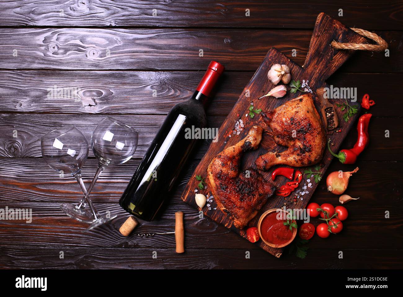 Gegrillte Hähnchenkeulen mit Gewürzen und Gemüse, dazu eine Flasche Rotwein. Stockfoto