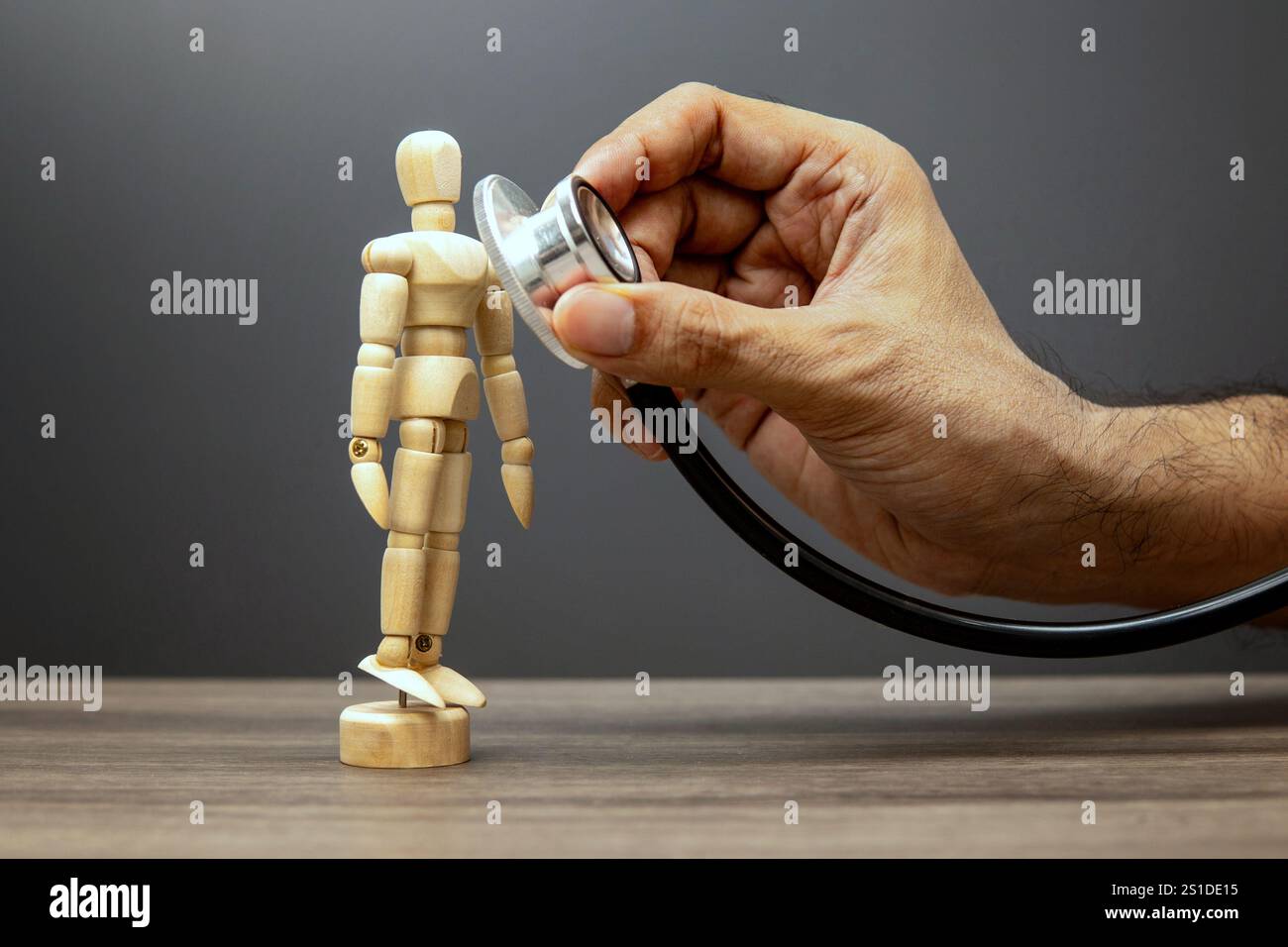 Eine Hand hält ein Stethoskop an der Brust einer hölzernen Schaufensterpuppe, symbolisiert Gesundheit und medizinische Untersuchung. Stockfoto
