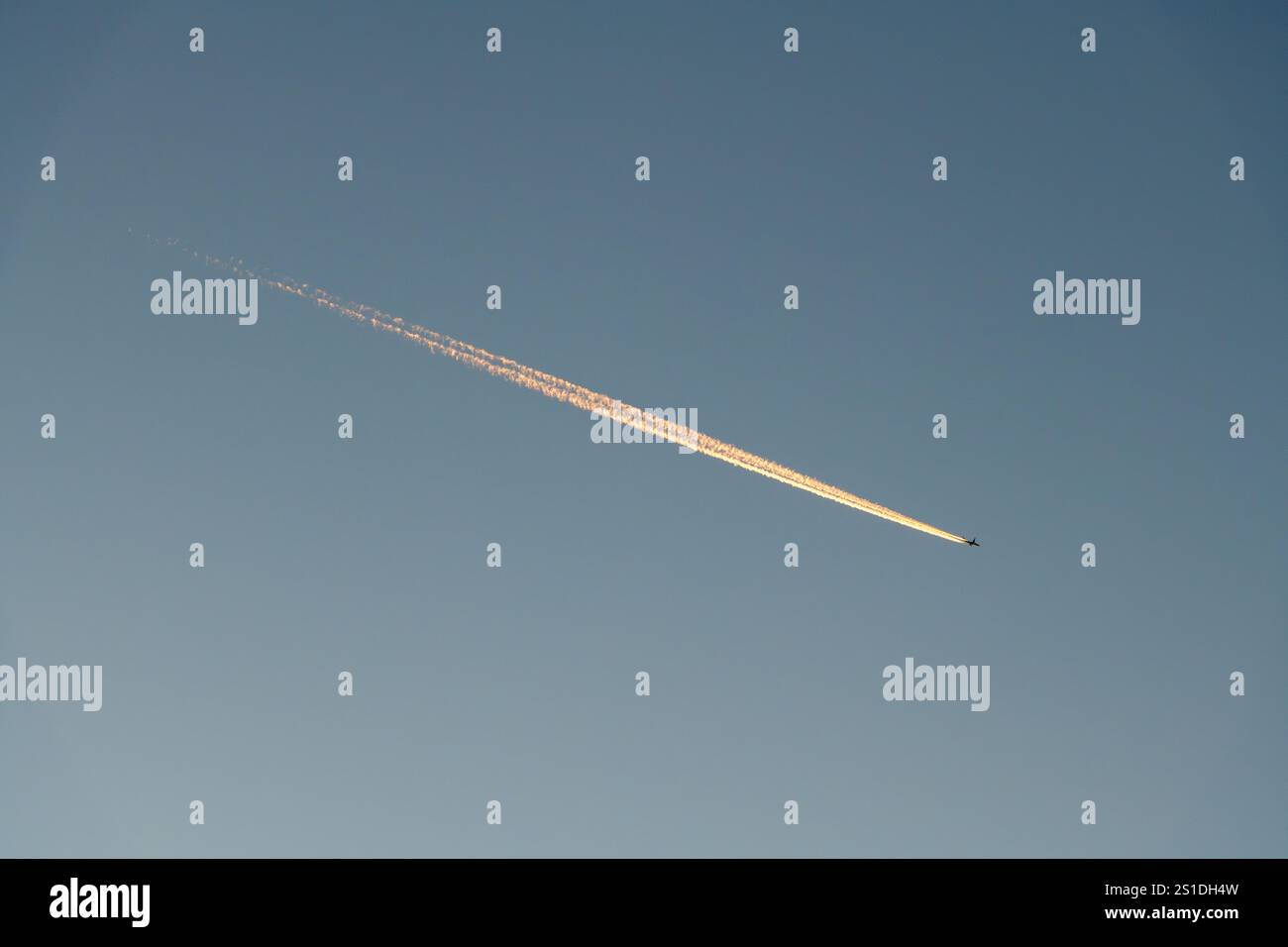 Ein Flugzeug und sein Kondensstreifen (Dampfspur), beleuchtet von der untergehenden Sonne, bei klarem Abendhimmel (UK) Stockfoto