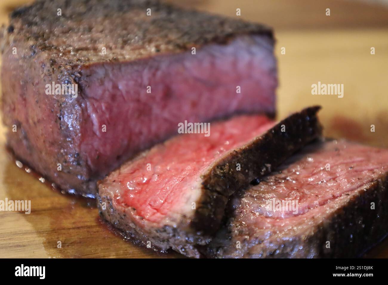 Saftige mittelseltene Steakscheiben mit einer gebratenen Kruste auf einem Holzbrett Stockfoto