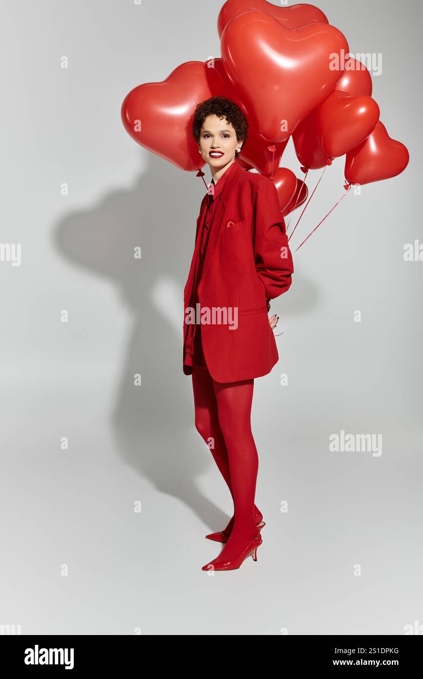 Eine stilvolle junge Frau posiert anmutig und hält helle, herzförmige Ballons in leuchtendem Rot. Stockfoto