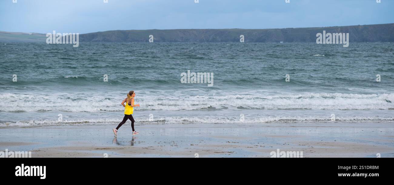 Ein Panoramabild einer einsamen Frau, die am Ufer des Towan Beach in Newquay Cornwall, Großbritannien, joggt. Stockfoto