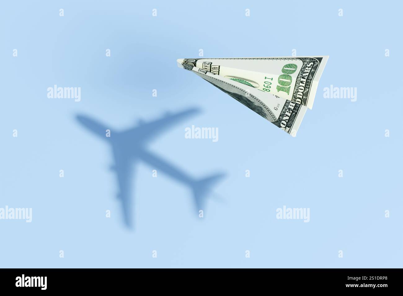 Papierflugzeug aus einem 100-Dollar-Schein, der über einem blauen Meer fliegt und einen realistischen kommerziellen Flugschatten projiziert. Stockfoto