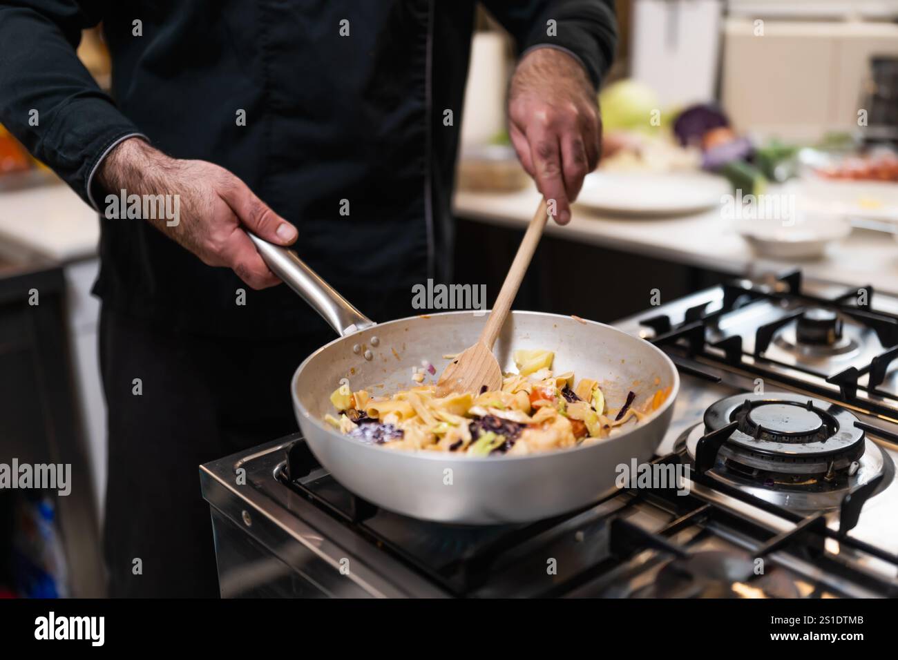 Nahaufnahme eines professionellen Küchenchefs, der vegetarische Gerichte mit einer Kelle in der Pfanne mischt. Stockfoto