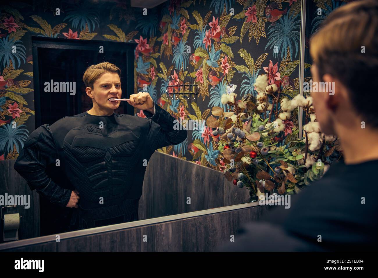 Mann, Superheld, der in den Spiegel blickt und Zähne putzt, ruhiger Fokus in einer lebendigen Umgebung, die banale mit achtsamer Entspannung verbindet. Stockfoto