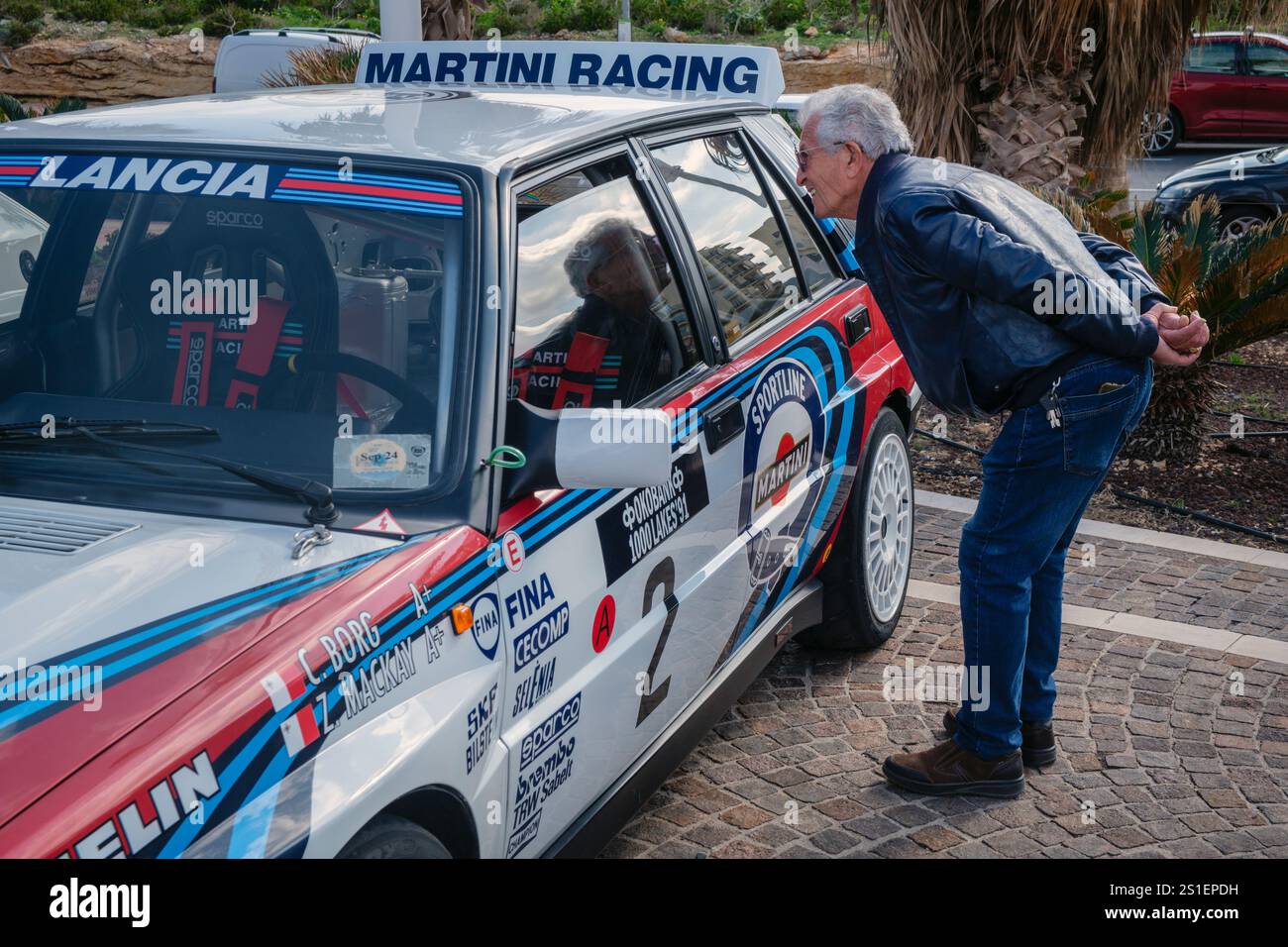 Ein Motorenfreund, der das Interieur eines Martini Racing Lancia bei einer Oldtimer-Rallye in Qawra, Malta, bewundert Stockfoto