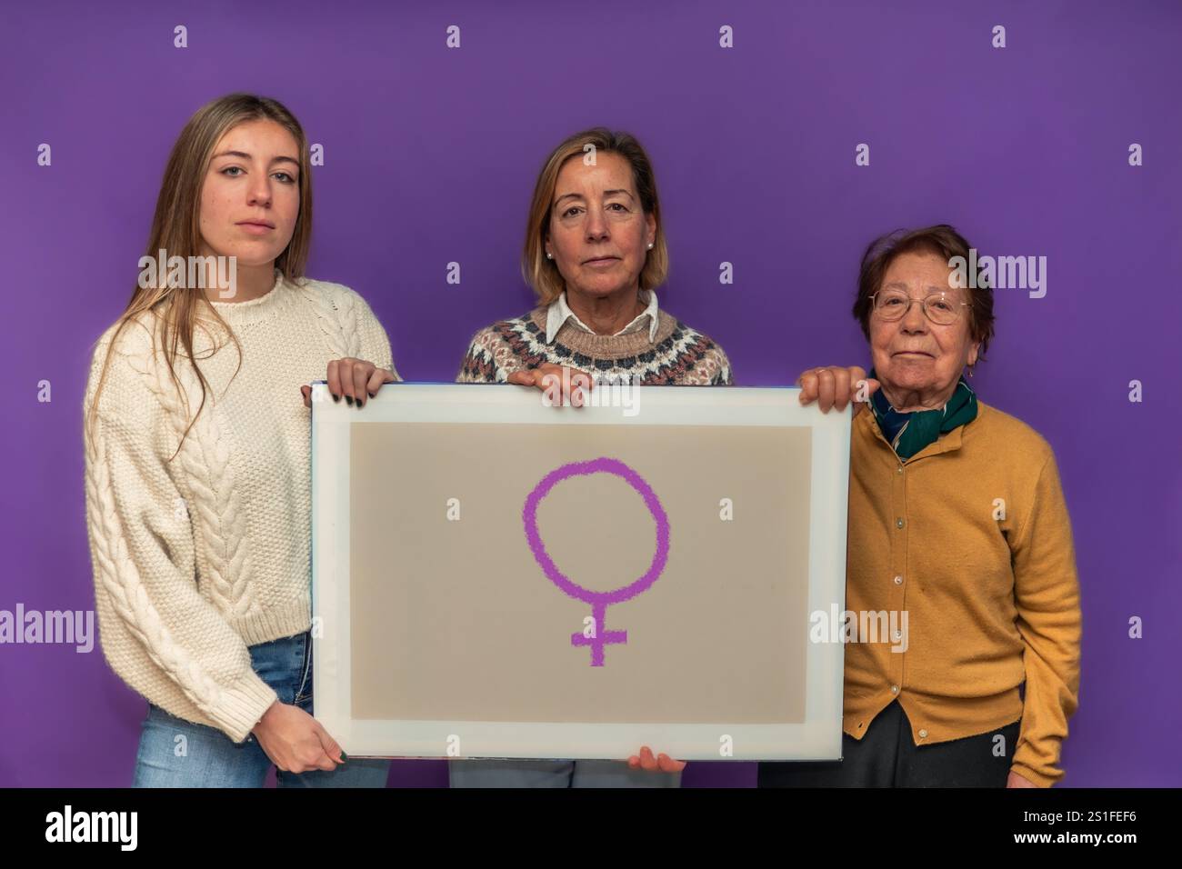 Drei Frauen unterschiedlichen Alters, die eine Leinwand mit dem weiblichen Symbol halten, feiern den Frauentag und die Macht der Frauen, Feminismus und Schwesternschaft. Stockfoto