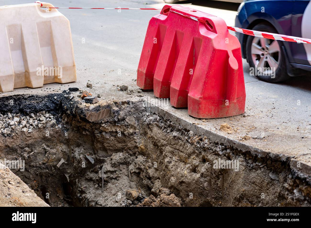 Entlang einer Stadtstraße ist ein großer Graben zu sehen, der von roten und weißen Barrieren markiert ist. Schwere Anlagen sind vorhanden, was auf eine laufende Baustelle hinweist Stockfoto