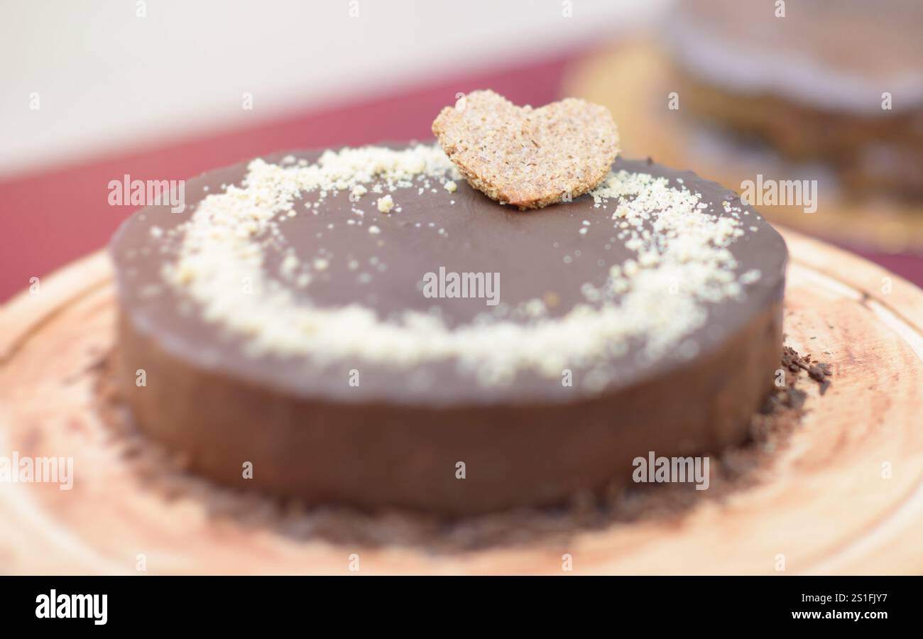 Ein köstlicher Schokoladenkuchen mit herzförmiger Keksdekoration auf einem Holzbrett. Der Kuchen ist mit Semmelbröseln garniert, Maki Stockfoto