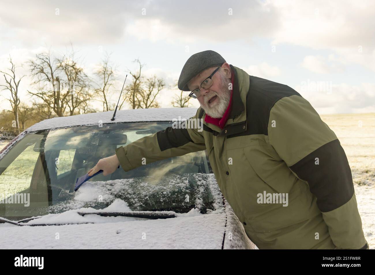 Seniorin entfernt Frost und Schnee von der Windschutzscheibe Stockfoto