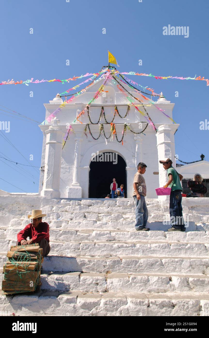 Kirche Capilla del Calvario Chichicastenango Guatemala // CHICHICASTENANGO, Guatemala — Ein Mann, der Feuerholz verkauft, liegt auf den Stufen der Capilla del Calvario, einer weiß getünchten Kirche im Zentrum von Chichicastenango, direkt gegenüber der Kirche Santo Tomas. Chichicastenango ist eine indigene Maya-Stadt im guatemaltekischen Hochland etwa 90 Meilen (145 km) nordwestlich von Guatemala-Stadt auf einer Höhe von fast 6.500 Fuß (1.980 Meter). Die Stadt ist bekannt für ihre lebhaften Märkte, die donnerstags und sonntags stattfinden und sowohl Einheimische als auch Touristen auf der Suche nach traditionellen Maya-Textilien und Kunsthandwerk anlocken Stockfoto