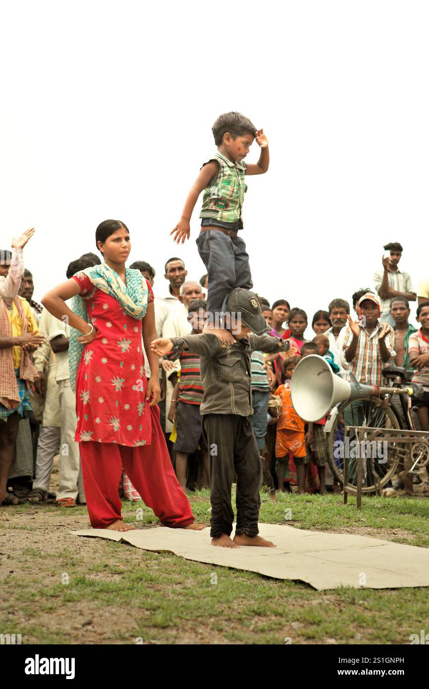 Kinder, die vor Dutzenden von Zuschauern auf einem Feld am Straßenrand am Stadtrand von Rajgir in Bihar, Indien, einen Gymnastikstunt durchführen. Stockfoto