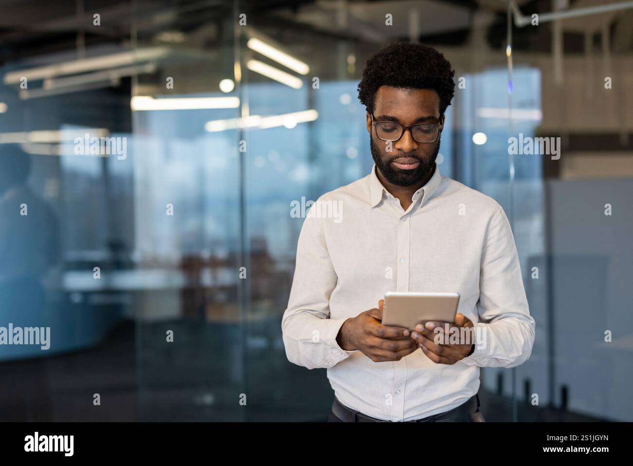Ernsthafter Geschäftsmann mit Tablet-Computer in der Hand. Junger Mann in Geschäftskleidung mit App, liest E-Mails und sieht Finanzdaten online an. Stockfoto