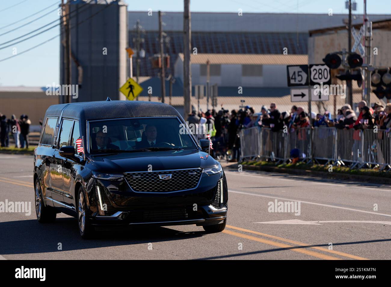 People watch as a hearse carrying the flag-draped casket of former President Jimmy Carter passes a grain elevator as it moves through downtown Plains, Ga., Saturday, Jan. 4, 2025. (AP Photo/Mike Stewart) Stockfoto