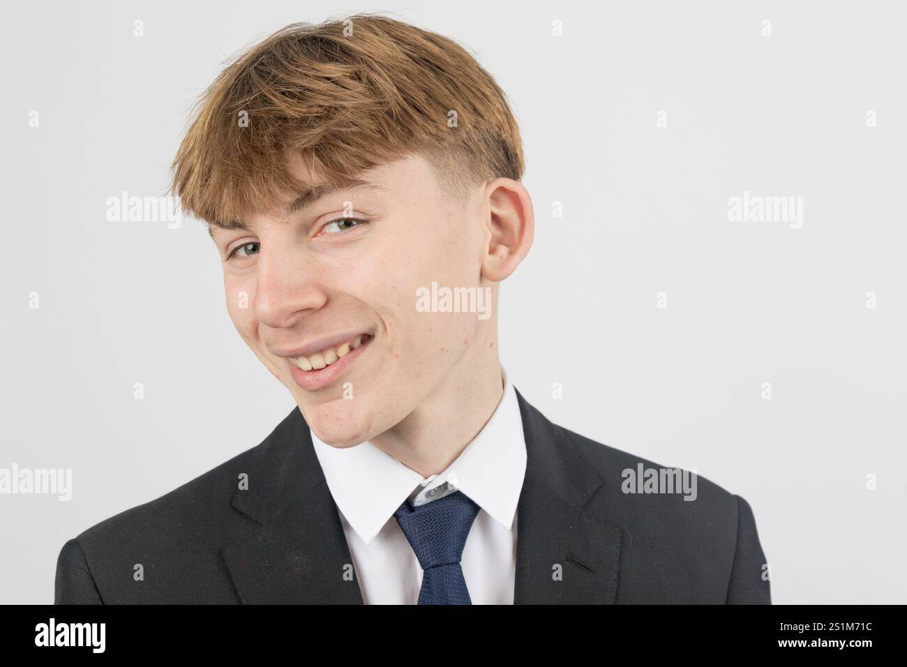 Glücklicher, sechzehnjähriger Teenager, der einen Anzug trägt, Studioaufnahme vor weißem Hintergrund Stockfoto