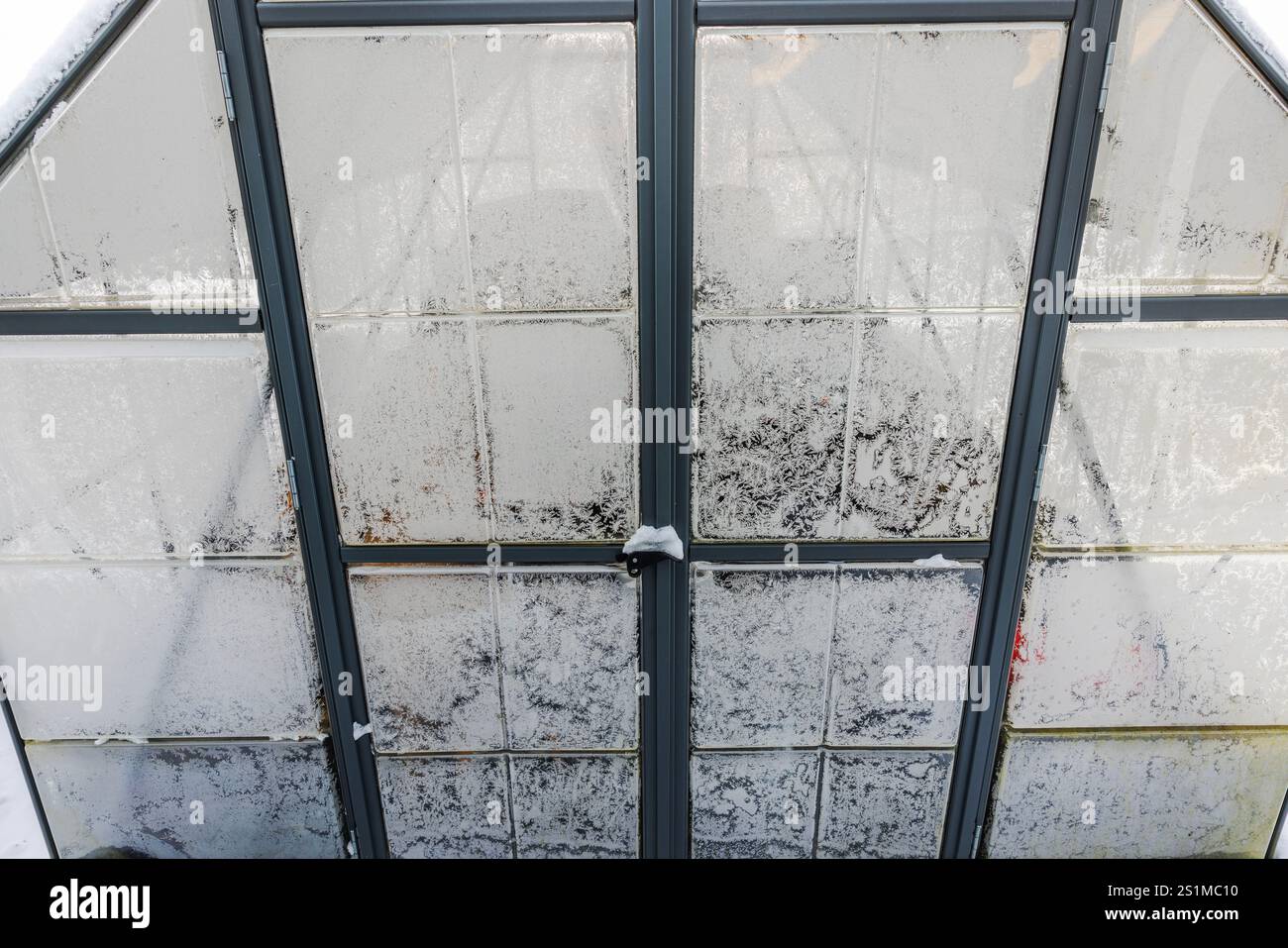 Milchglasscheiben mit verflochtenen Eismustern und Schneefall auf Metallrahmen im Winter. Stockfoto