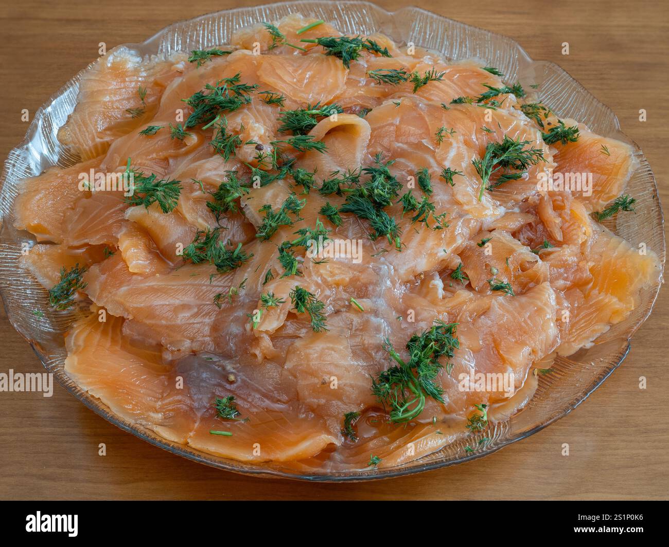 Dünn geschnittene Gravlax, geräucherter Lachs mit Dill, ist elegant auf einer Glasplatte angeordnet und servierfertig. Stockfoto