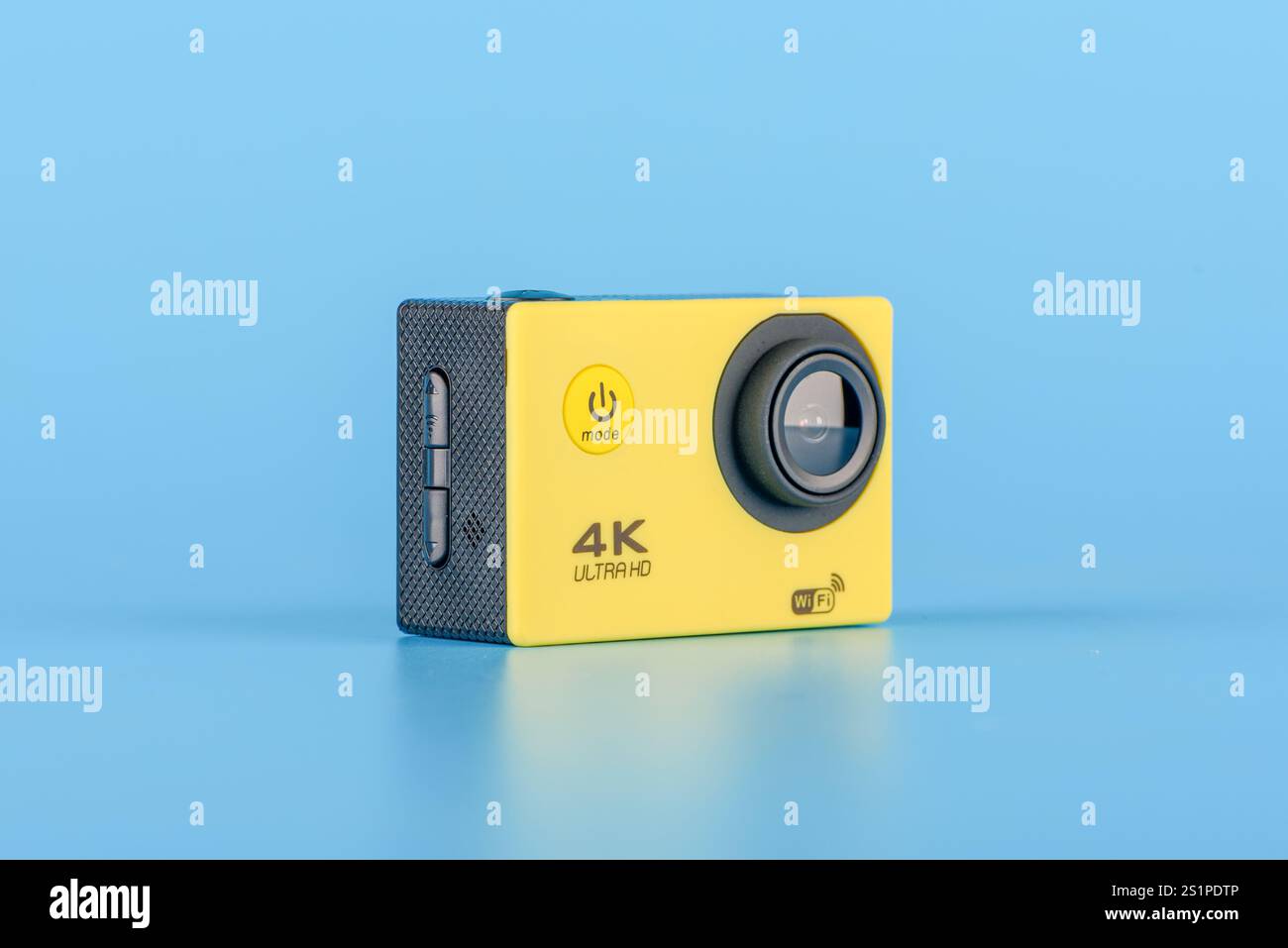 Moskau, Russland - 3. Januar 2025: Kompakte gelbe 4K-Action-Kamera mit Objektiv und Tasten auf blauem Hintergrund, die moderne Technologie repräsentiert Stockfoto