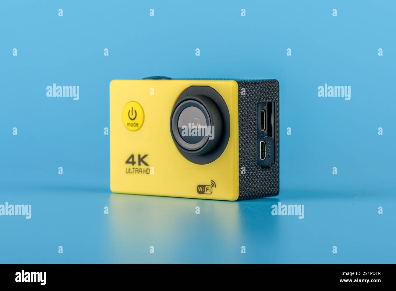 Moskau, Russland - 3. Januar 2025: Gelbe 4K-Action-Kamera mit Objektiv und Ports, minimalistischer Stil, auf blauem Hintergrund stehend, Konzept der Technologie und Stockfoto