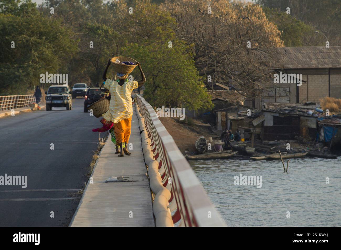 Rückansicht einer typischen afrikanerin, die mit einem Kopf über die Brücke über den Casamance River in Zuiguinchor, Senegal, läuft. Typisch afrikanisches Gefühl Stockfoto