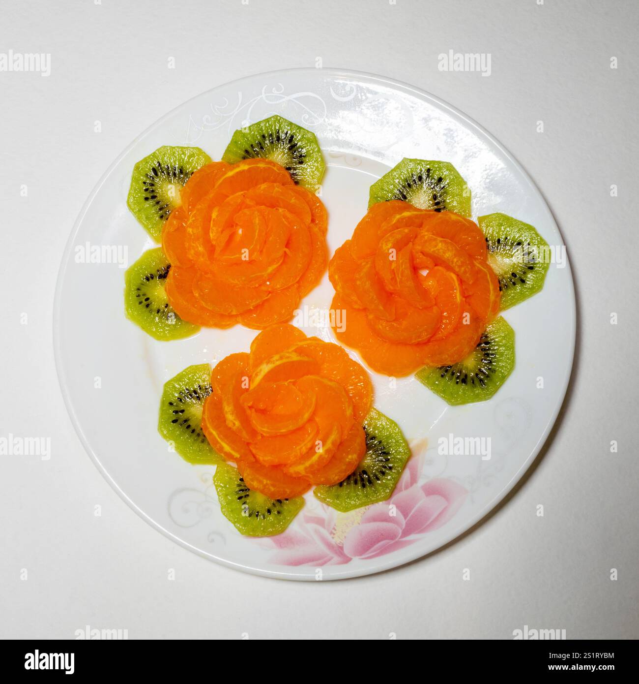 Ein wunderschön angeordneter Teller zeigt drei rosenförmige Mangoblätter, umgeben von sechseckigen Kiwi-Stücken. Die lebendigen Farben sorgen für eine ansprechende PR Stockfoto