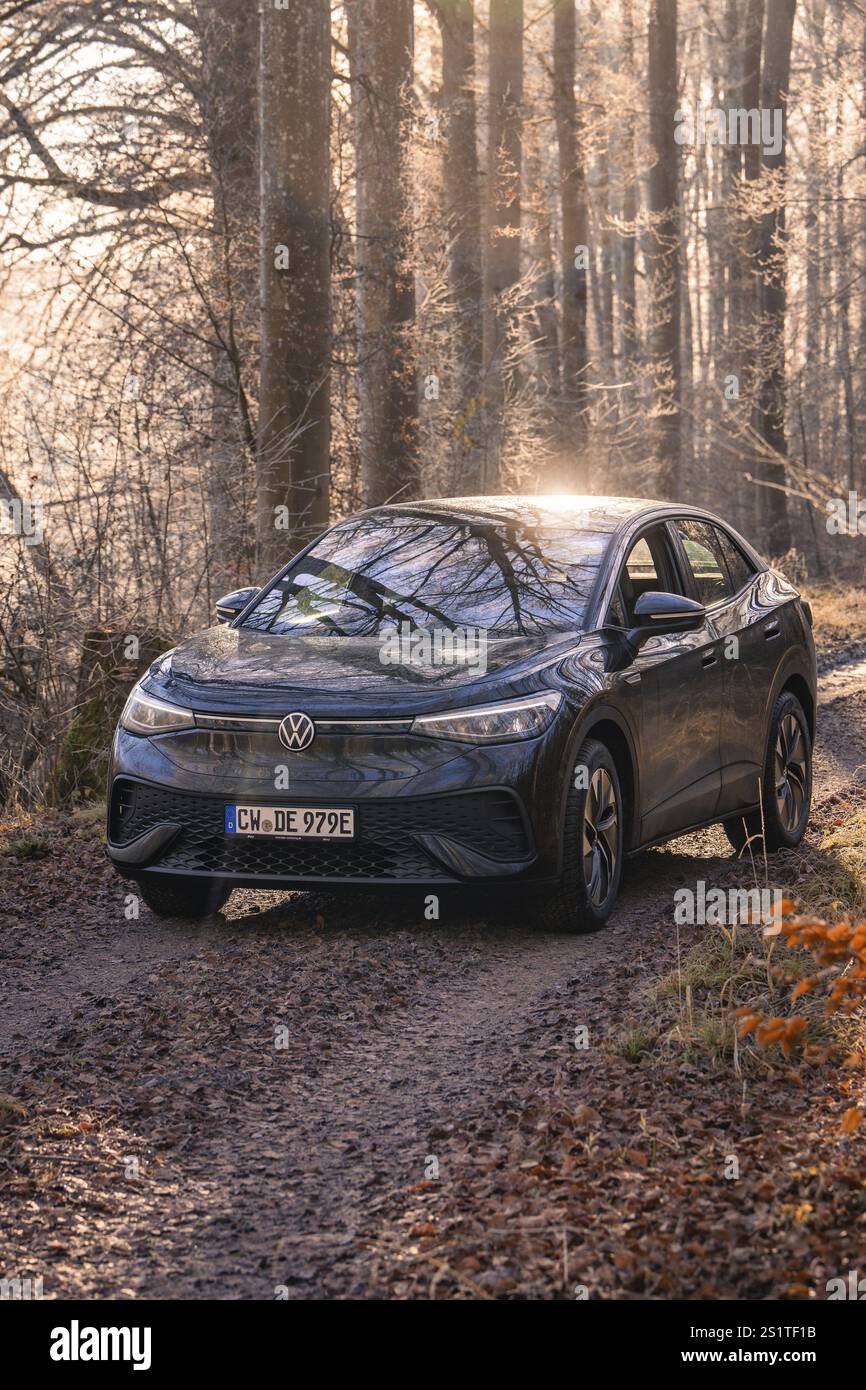 Auto fährt durch einen schattigen Waldweg im Sonnenlicht, Car Sharing, Elektroauto, Volkswagen ID 5, Gechingen, Region Hecken und Gaeu, Schwarzwald, Keim Stockfoto