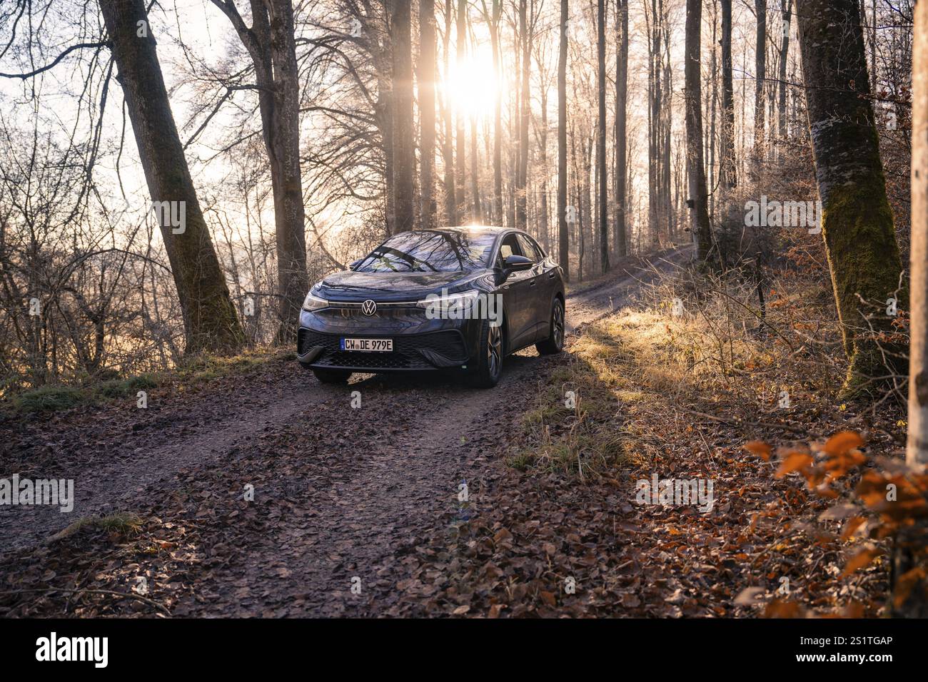 Fahrzeug auf einem Waldweg, beleuchtet durch Sonnenlicht durch die Bäume, Carsharing, Elektroauto, Volkswagen ID 5, Gechingen, Region Hecken und Gaeu, BL Stockfoto