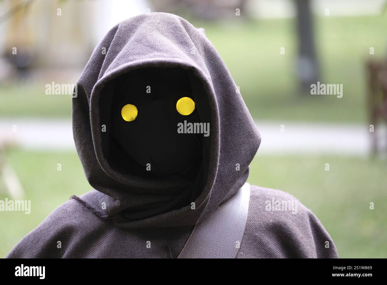 Eine geheimnisvolle Kapuzenfigur mit hellgelben Augen vor einem verschwommenen Hintergrund Stockfoto