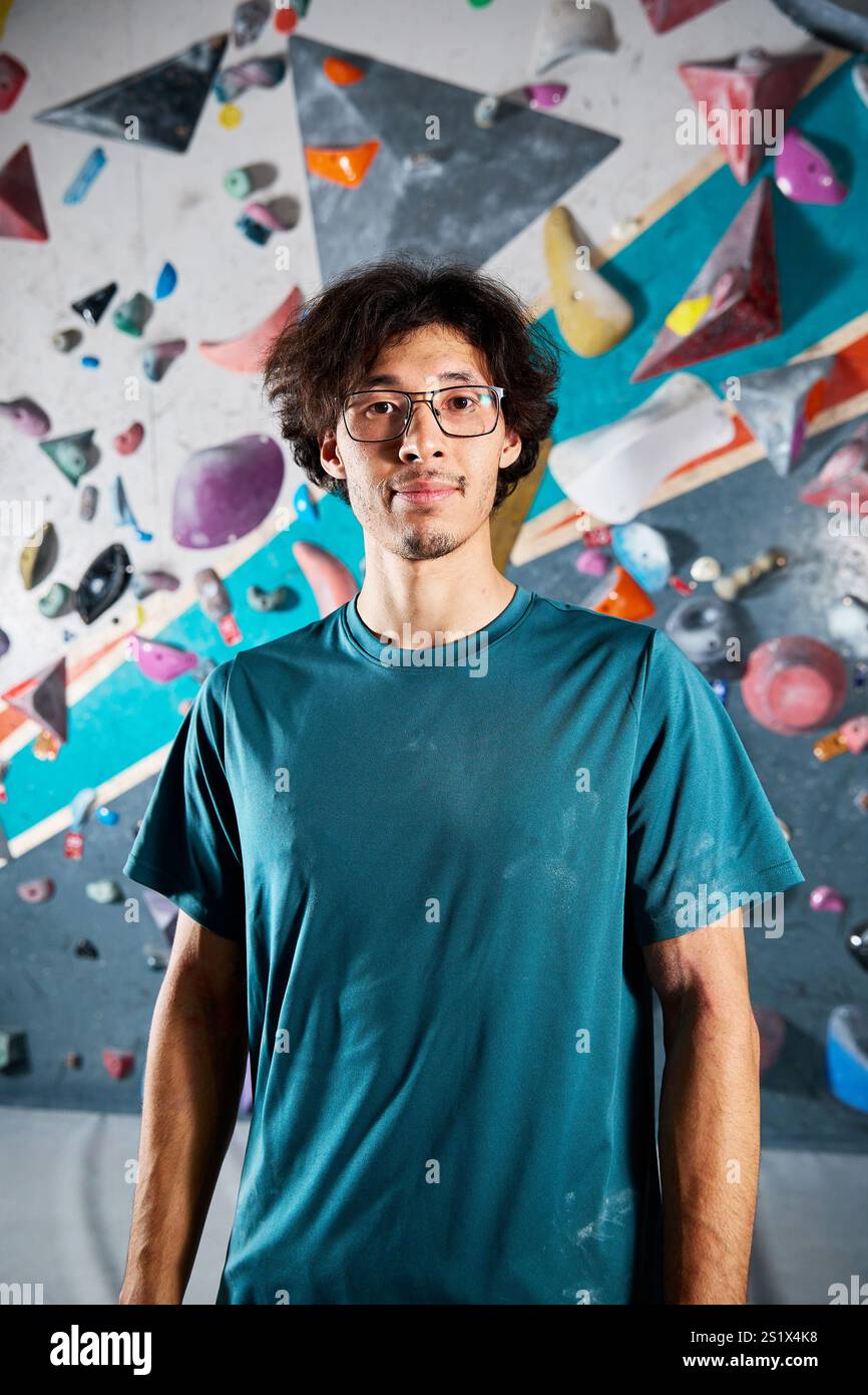 Sportlersportler Kletterporträt vor steiler Wand in Kletterhalle drinnen. Extremsport und Boulderkonzept Stockfoto