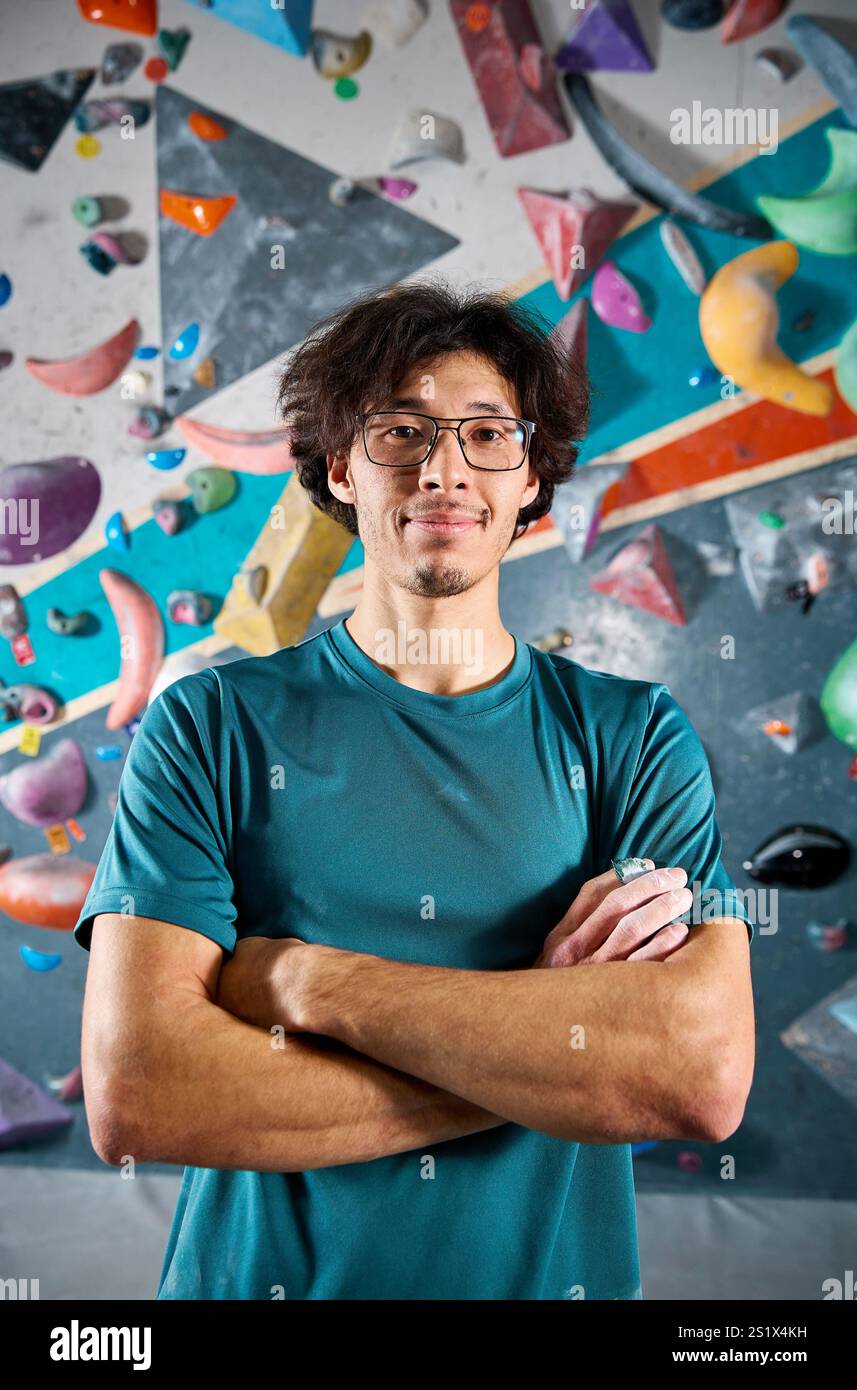 Sportlersportler Kletterporträt vor steiler Wand in Kletterhalle drinnen. Extremsport und Boulderkonzept Stockfoto