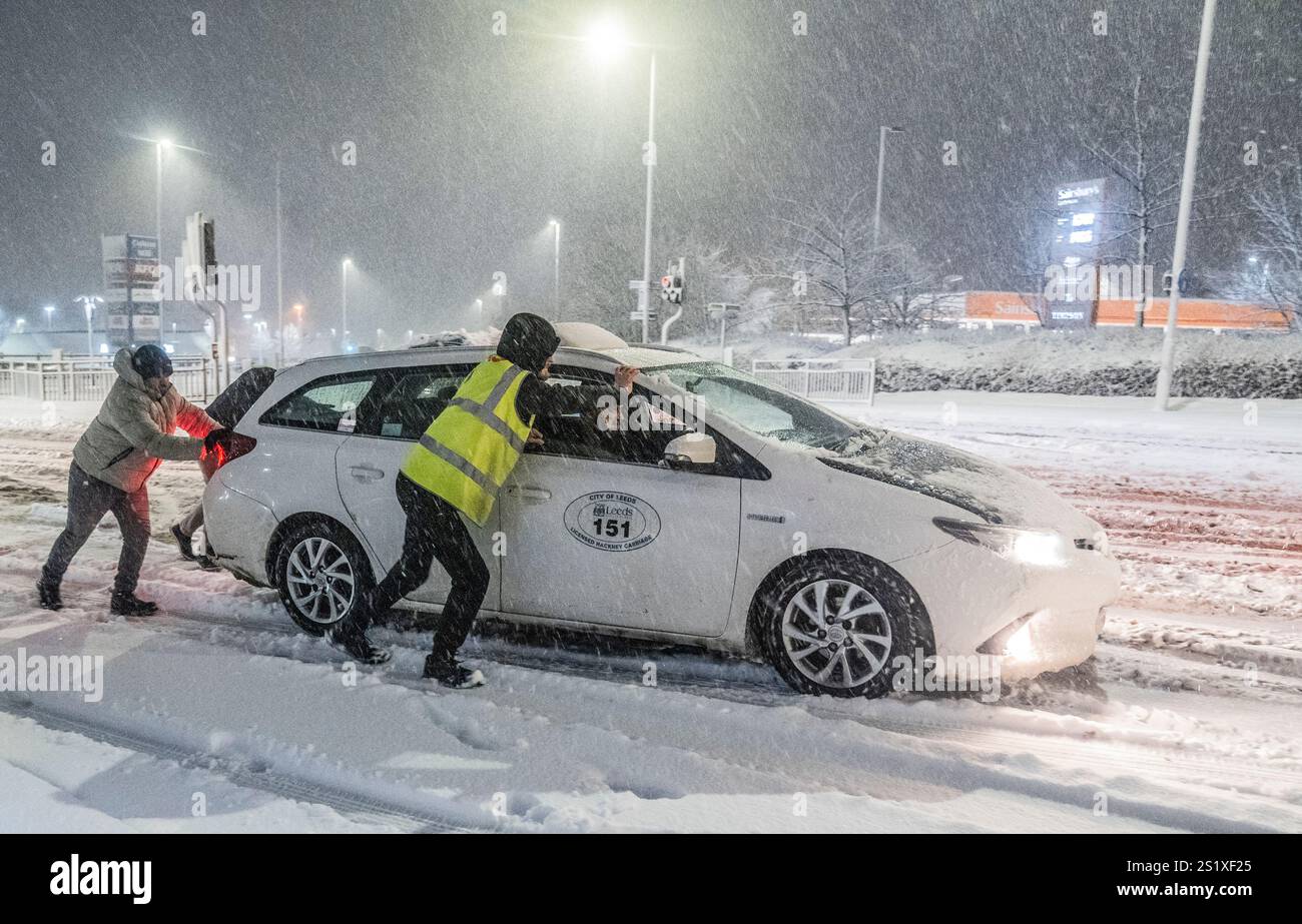Leute helfen, Autos im Schnee in Leeds, Yorkshire, zu schieben. Starker nächtlicher Schnee sorgt für Störungen in ganz Großbritannien, da der Kaltstart ins neue Jahr anhält. Bilddatum: Sonntag, 5. Januar 2025. Stockfoto