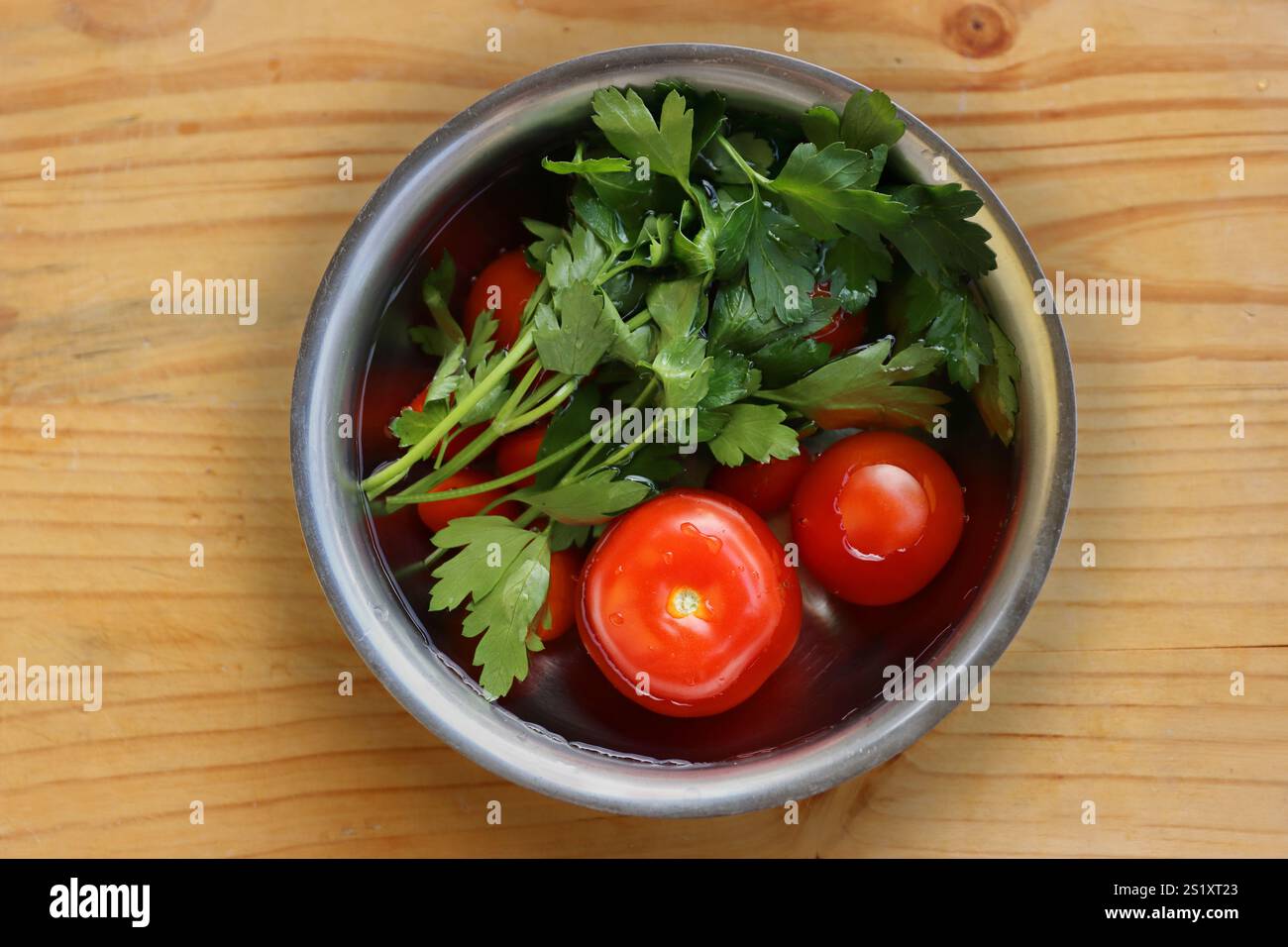 Frisches Gemüse wird in der Metallschale gewaschen, die mit kaltem Wasser gefüllt ist, auf dem Vintage-Schneidebrett aus zerrissenem Holz. Bio-Tomaten, Petersilie, ce Stockfoto