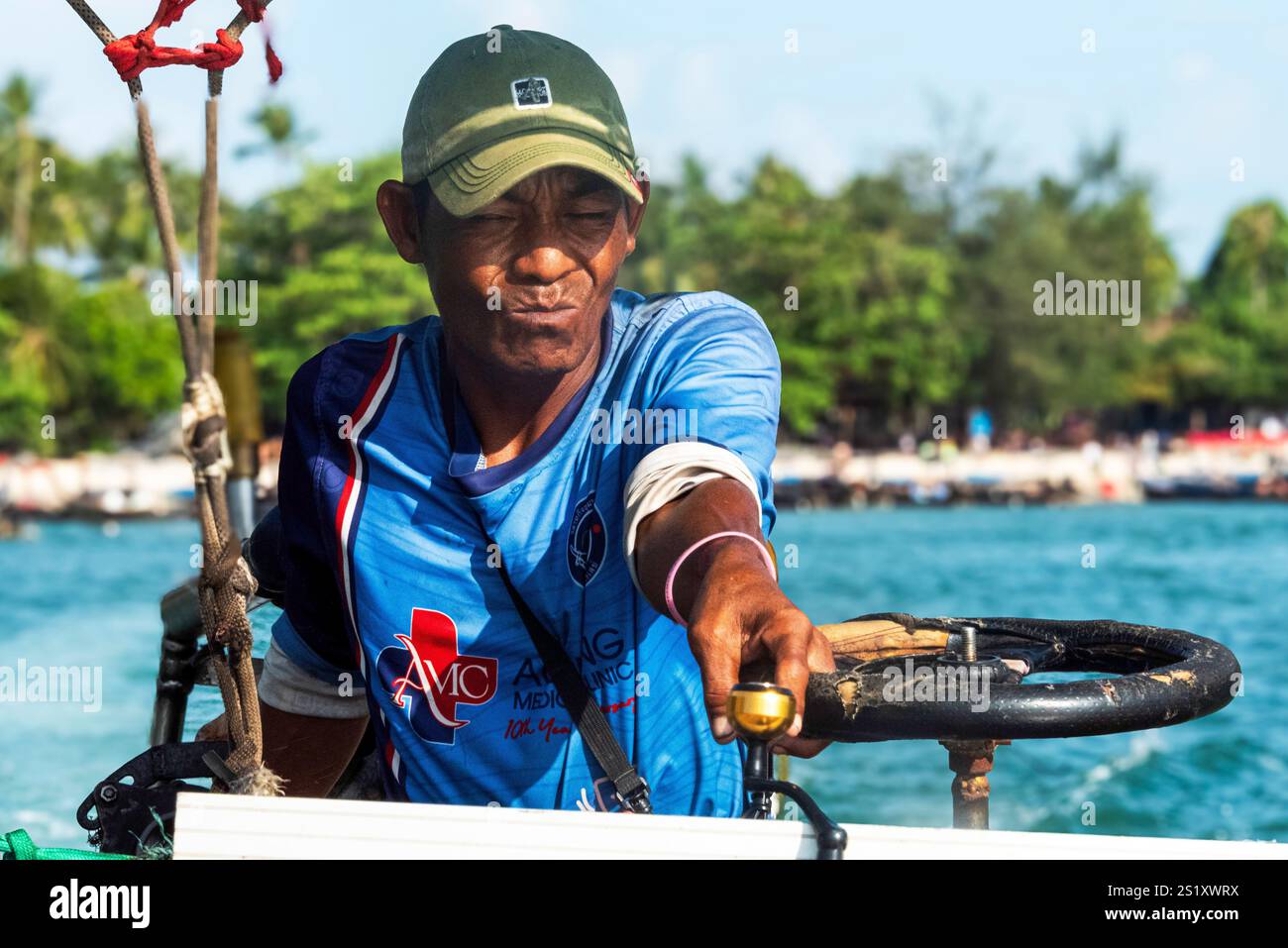 Erfahrener Langboot-Fahrer in einem blauen Hemd und Hut, der geschickt durch die tropischen Gewässer Thailands fährt und das Wesen des Autors erfasst Stockfoto